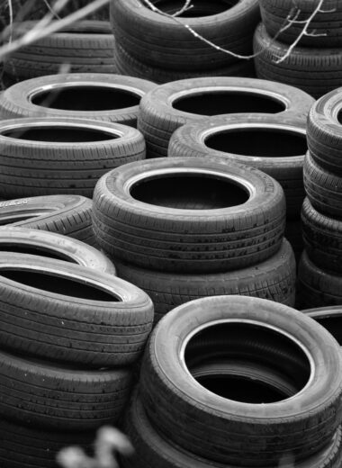 A vertical black and white photograph of stacked car tires in an outdoor setting.